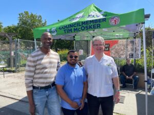 Three men stand outstide in front of a informational tent at a Cesar Chavez Day event in 2023.