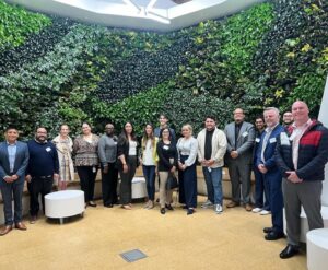 A line of individuals in an office setting, in front of a wall of live plants.