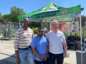 Three men stand outstide in front of a informational tent at a Cesar Chavez Day event in 2023. 